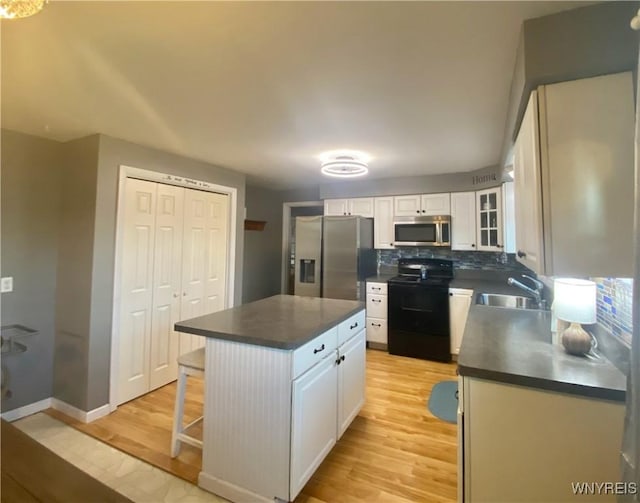 kitchen with stainless steel appliances, dark countertops, light wood finished floors, and white cabinetry
