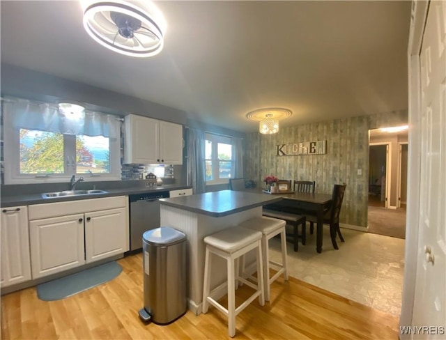 kitchen featuring dishwasher, a sink, dark countertops, white cabinetry, and a breakfast bar area