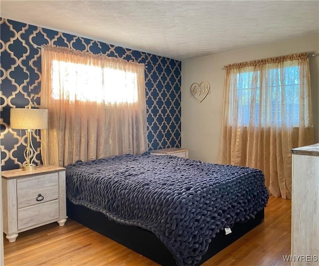 bedroom with wallpapered walls, wood finished floors, multiple windows, and a textured ceiling