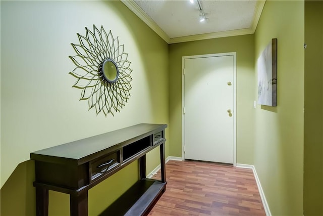 doorway to outside featuring track lighting, wood finished floors, ornamental molding, and baseboards