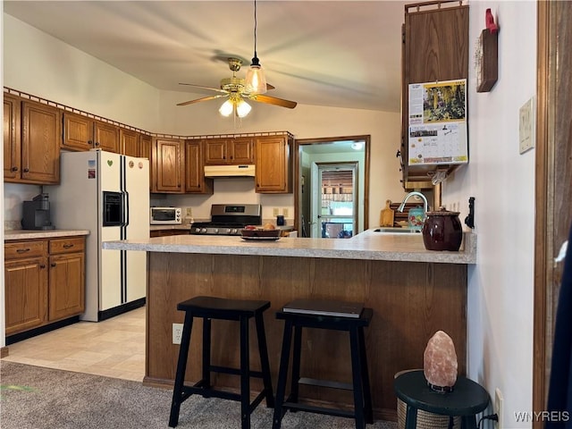 kitchen featuring white refrigerator with ice dispenser, a sink, gas stove, under cabinet range hood, and a ceiling fan