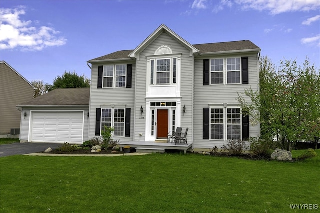 colonial home featuring an attached garage, driveway, a front yard, and central air condition unit