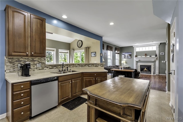 kitchen with stainless steel dishwasher, a sink, a lit fireplace, tasteful backsplash, and light countertops