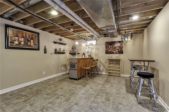 basement featuring a bar, baseboards, and stone finish floors
