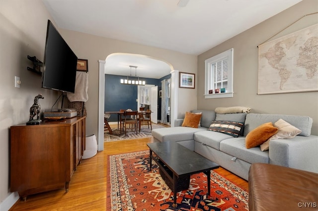 living area with arched walkways, light wood-type flooring, and a chandelier