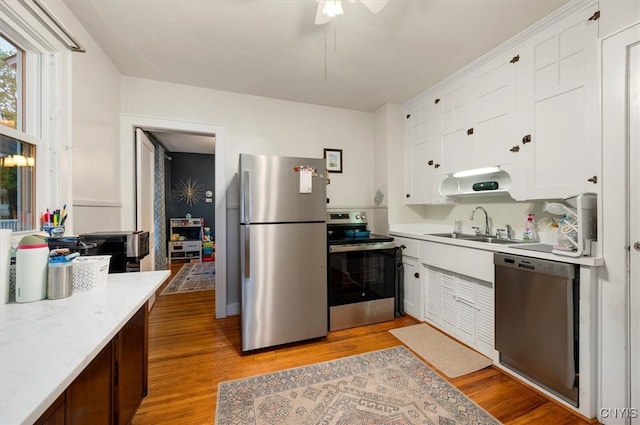 kitchen featuring appliances with stainless steel finishes, a sink, light countertops, light wood-style floors, and white cabinetry