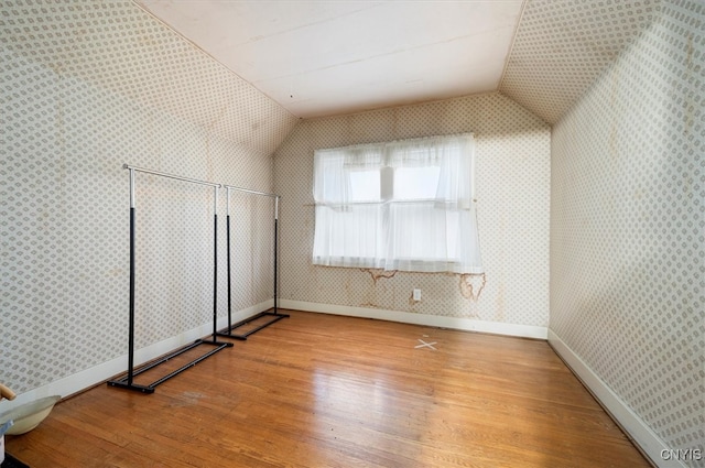 bonus room featuring wood finished floors, wallpapered walls, vaulted ceiling, and baseboards