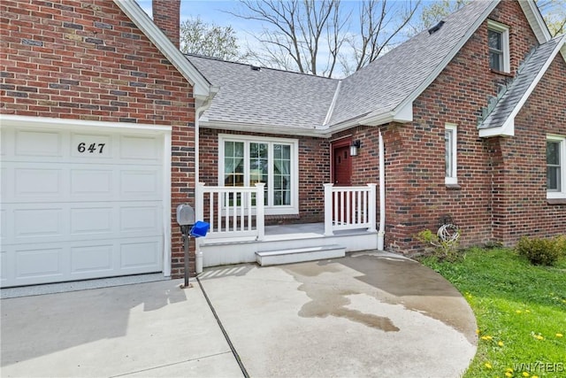 entrance to property with a shingled roof, brick siding, a chimney, a garage, and driveway