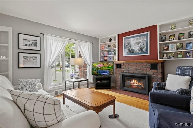 living area with wood finished floors, a brick fireplace, and built in features