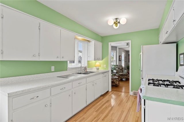 kitchen with white appliances, a sink, light wood finished floors, and white cabinets