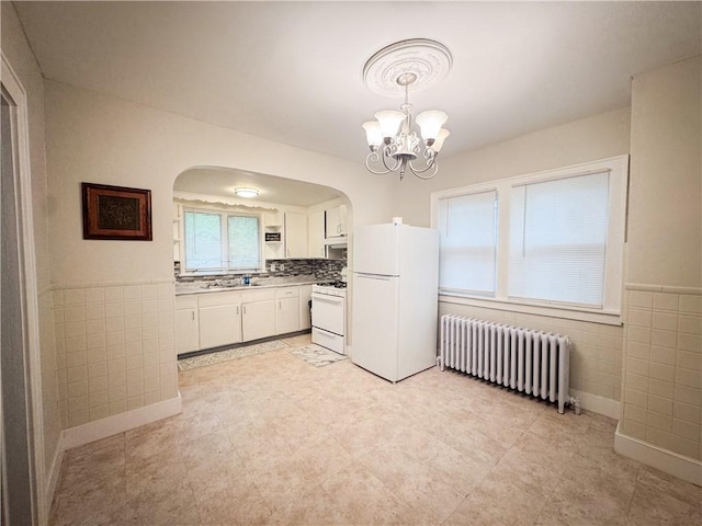 kitchen with radiator heating unit, white appliances, arched walkways, white cabinets, and tile walls