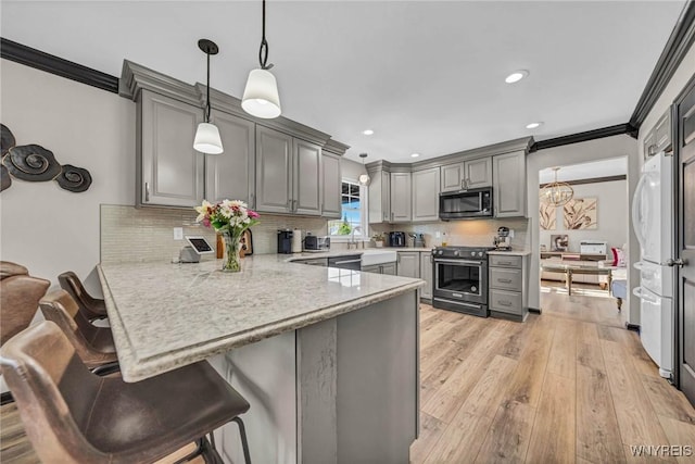 kitchen featuring stainless steel appliances, gray cabinets, ornamental molding, a peninsula, and light wood-type flooring