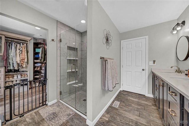full bath featuring a stall shower, baseboards, a walk in closet, double vanity, and recessed lighting