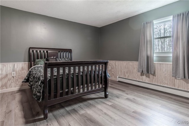 30204 County Route 179, Lyme, NY 13622 - bedroom with a baseboard radiator, wainscoting, wood finished floors, wooden walls, and a textured ceiling