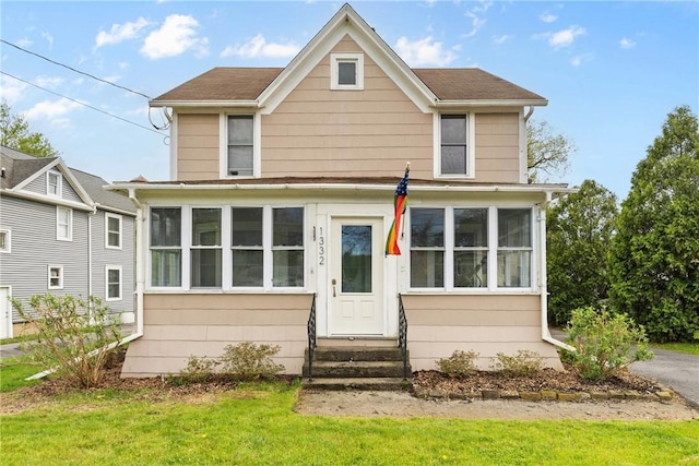 view of front of home with a sunroom, entry steps, roof with shingles, and a front yard