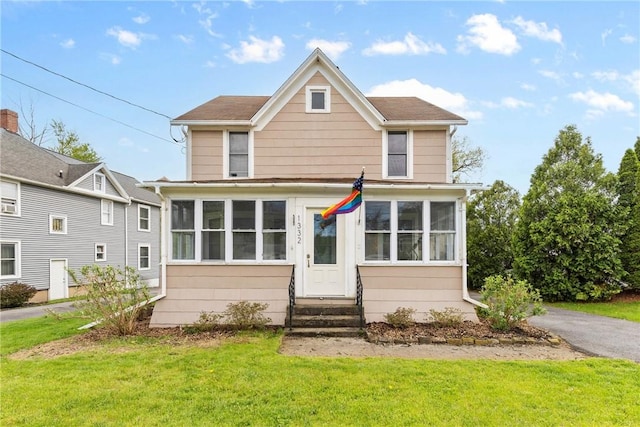 view of front of home featuring entry steps, a sunroom, and a front lawn