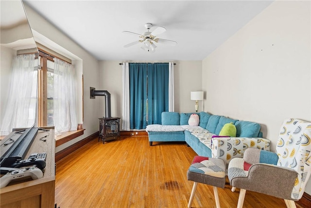 living area with a wood stove, a ceiling fan, light wood-type flooring, and baseboards