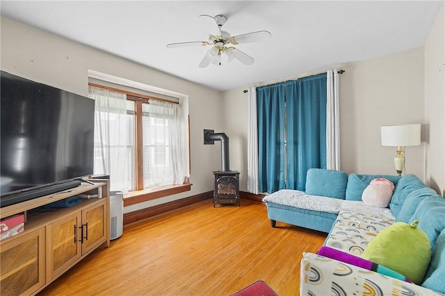 living area with a wood stove, light wood-style flooring, ceiling fan, and baseboards
