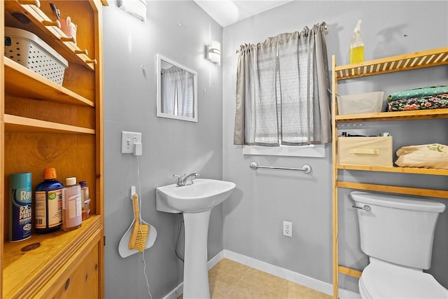 half bathroom with toilet, tile patterned floors, a sink, and baseboards