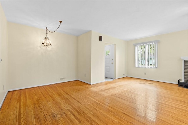 unfurnished living room featuring a chandelier, light wood-type flooring, a fireplace with raised hearth, and baseboards