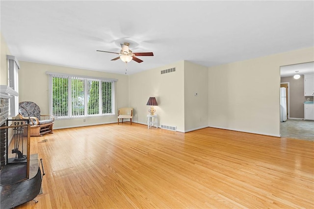 unfurnished living room featuring light wood-style floors, ceiling fan, a fireplace with raised hearth, and baseboards