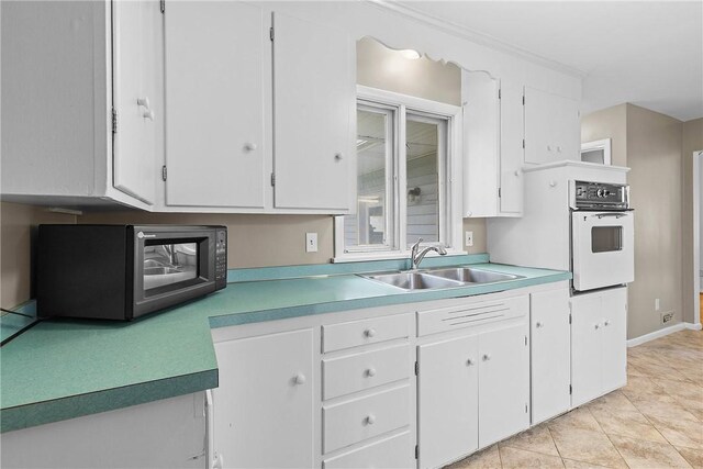 kitchen featuring white oven, white cabinetry, a sink, and light countertops