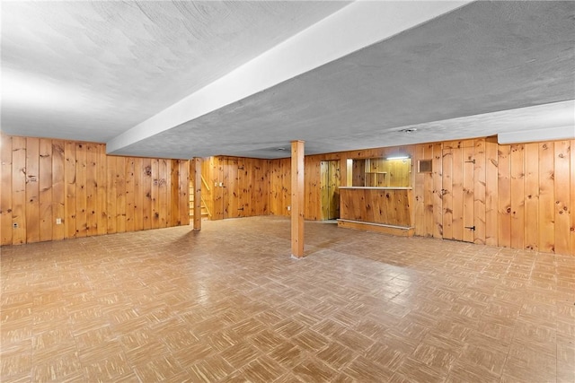 finished below grade area with wood walls, a textured ceiling, and parquet flooring