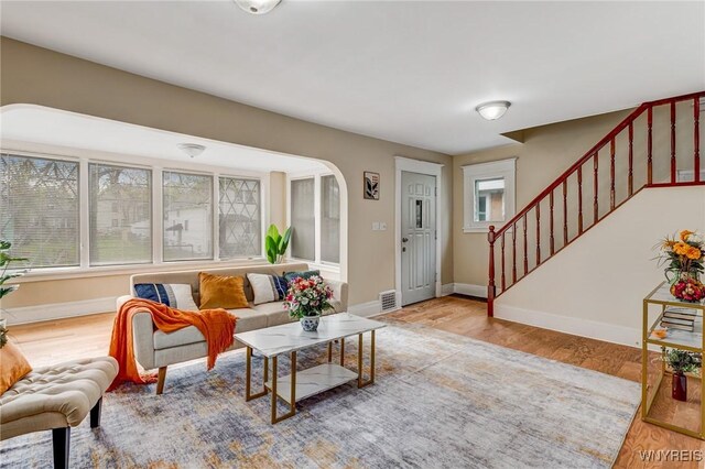 living room featuring stairway, wood finished floors, baseboards, and arched walkways