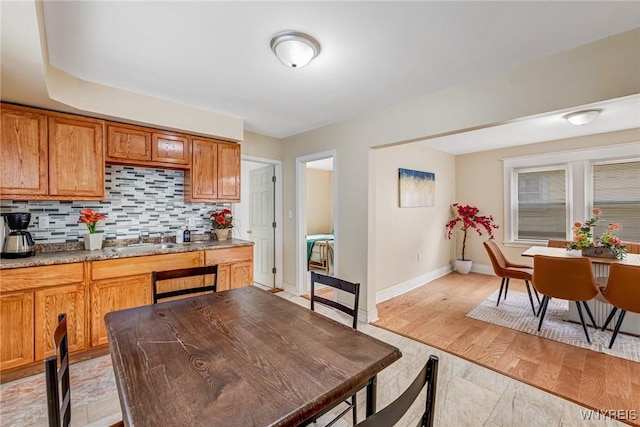 kitchen featuring a sink, tasteful backsplash, baseboards, and brown cabinetry