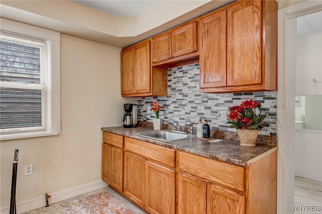 kitchen with a sink, decorative backsplash, dark countertops, and brown cabinets