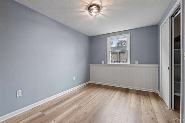 614 E Broadway St, Fulton, NY 13069 - unfurnished bedroom with light wood-type flooring, a textured ceiling, a closet, a wainscoted wall, and baseboards