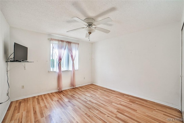 spare room with light wood-style floors, a ceiling fan, a textured ceiling, and baseboards