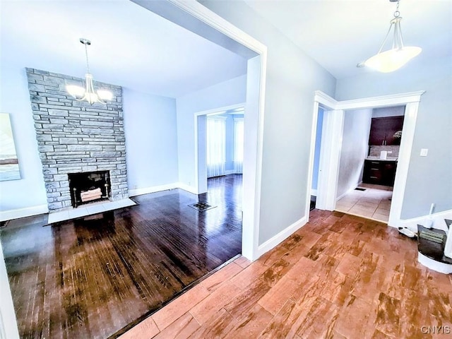 unfurnished living room with wood finished floors, a chandelier, a stone fireplace, and baseboards