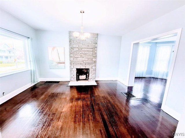 unfurnished living room featuring wood finished floors, a chandelier, a stone fireplace, and baseboards