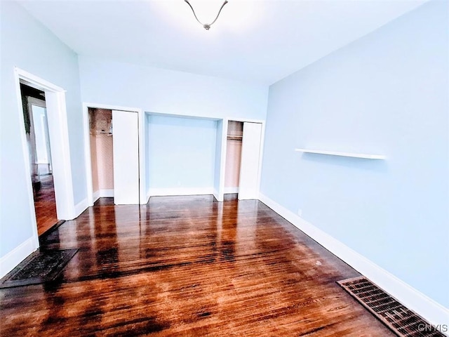 unfurnished bedroom featuring multiple closets, wood finished floors, and baseboards