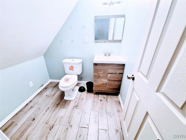 half bathroom with toilet, vanity, wood finished floors, baseboards, and vaulted ceiling