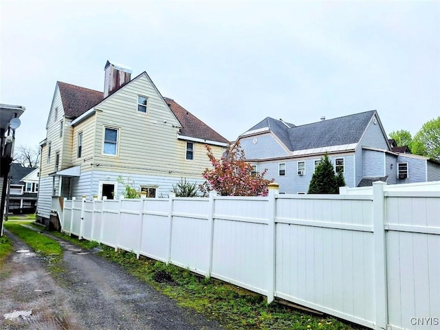 view of property exterior with fence, a chimney, and roof with shingles