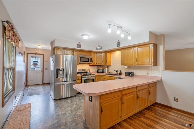 kitchen with appliances with stainless steel finishes, a sink, light countertops, a peninsula, and decorative backsplash