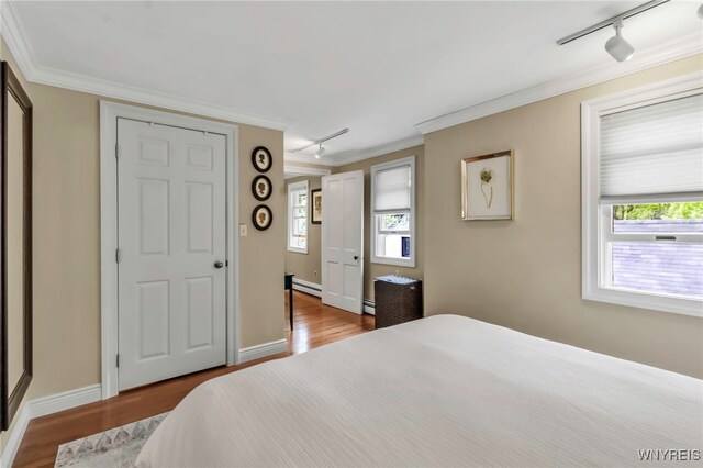 bedroom with track lighting, ornamental molding, a baseboard radiator, wood finished floors, and multiple windows