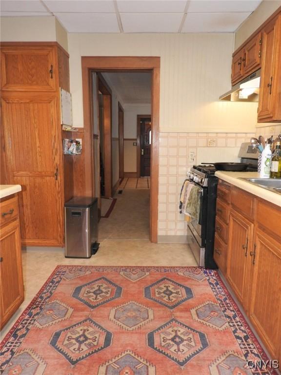 23 Paul St, Auburn, NY 13021 - kitchen with stainless steel gas stove, under cabinet range hood, light countertops, brown cabinetry, and light floors