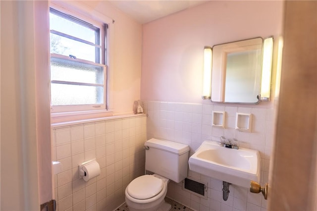 half bathroom with toilet, tile walls, wainscoting, and a sink