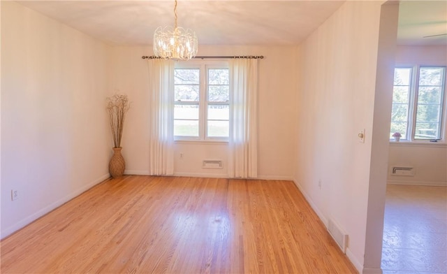 empty room with healthy amount of natural light, a chandelier, light wood-style flooring, and baseboards