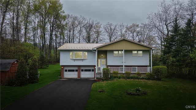 bi-level home featuring driveway, a front lawn, an attached garage, metal roof, and covered porch