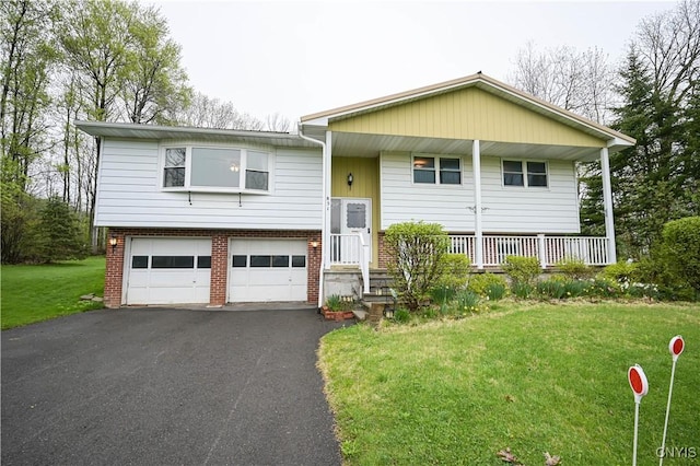 split foyer home featuring asphalt driveway, an attached garage, a front yard, brick siding, and covered porch