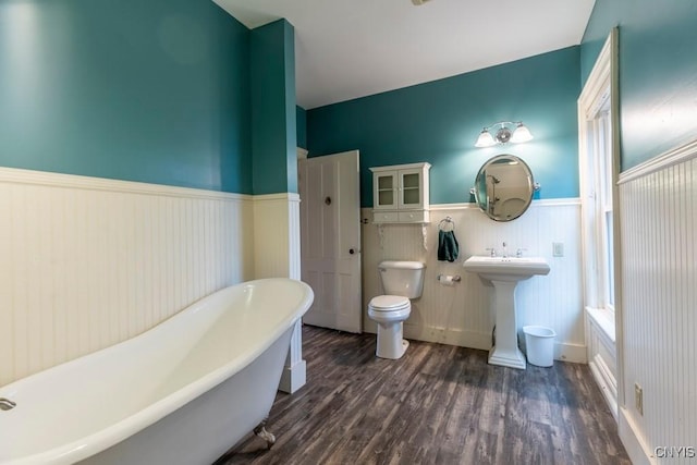 1957 Torpy Pond Rd, Georgetown, NY 13061 - bathroom featuring wainscoting, wood finished floors, a freestanding bath, toilet, and a sink