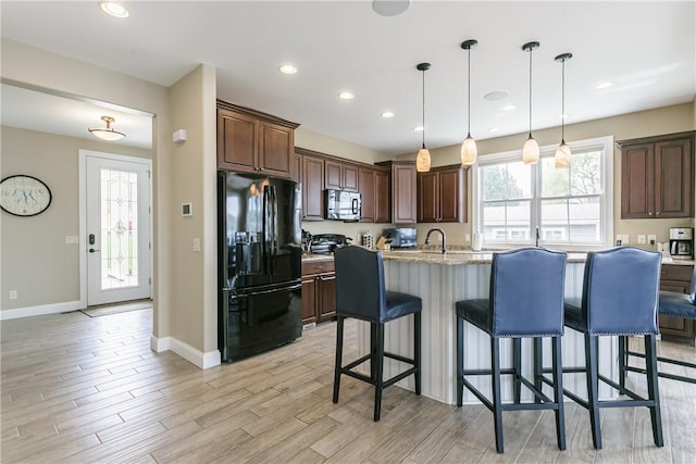 5088 E Lake Rd, Gorham, NY 14544 - kitchen featuring black fridge with ice dispenser, stainless steel microwave, baseboards, a center island with sink, and a kitchen bar