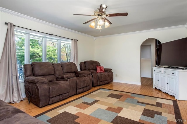 living area featuring light wood-type flooring, arched walkways, ornamental molding, ceiling fan, and baseboards