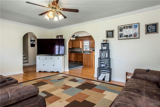 living room with a ceiling fan, arched walkways, light wood-style floors, ornamental molding, and stairway