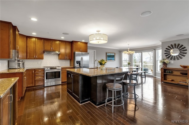 kitchen with appliances with stainless steel finishes, a sink, brown cabinets, a chandelier, and crown molding