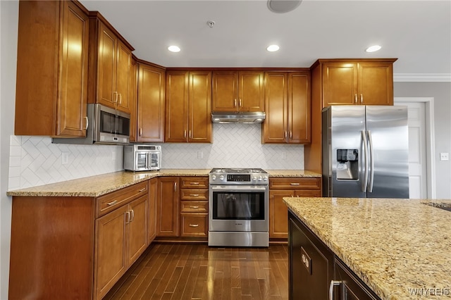 kitchen featuring appliances with stainless steel finishes, under cabinet range hood, light stone countertops, dark wood-style flooring, and brown cabinets